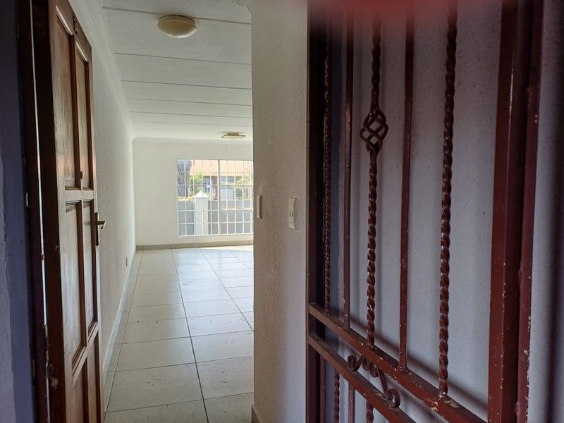 An entry area featuring tiled flooring, a security gate, and a window with burglar bars, leading into an open, vacant living space.