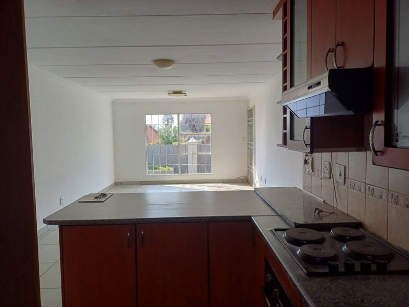 Open-plan kitchen and living area featuring built-in cabinetry, electric hob, extractor fan, and tiled flooring, offering a bright and functional space.