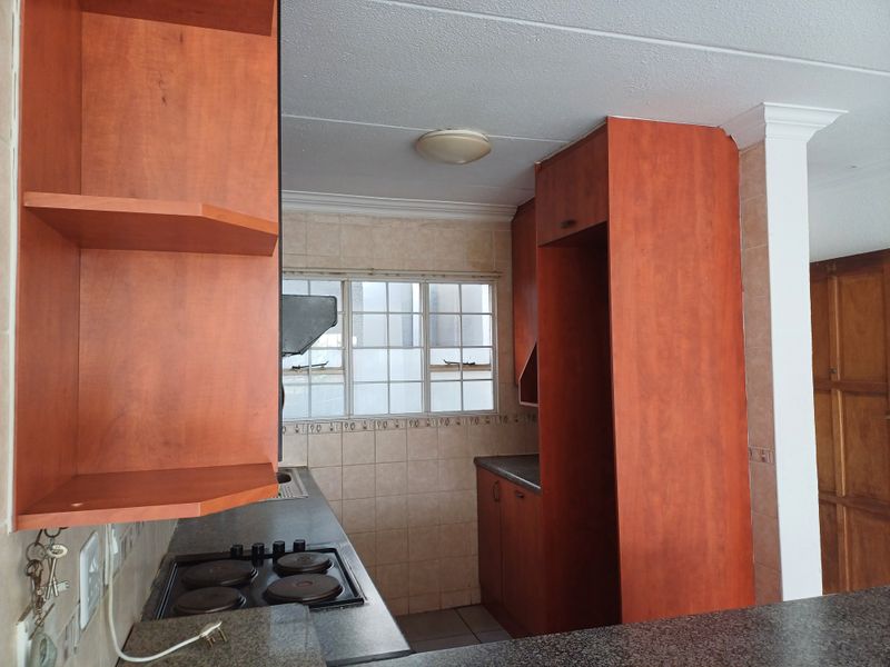 A functional kitchen featuring built-in wooden cabinetry, an electric hob, tiled backsplash, and ample counter space, offering a practical layout for daily use.