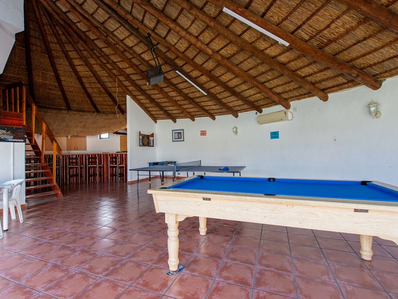 Spacious entertainment area featuring a high thatched roof with exposed rafters, built-in bar counter, and tiled flooring, ideal for social gatherings.