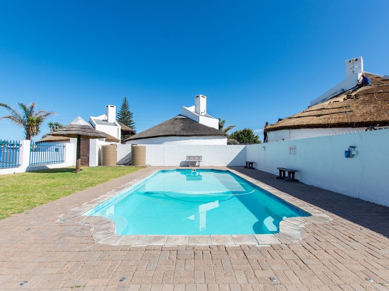 Outdoor pool area featuring paved surround, boundary walls, and adjacent thatched roof buildings under maintenance.