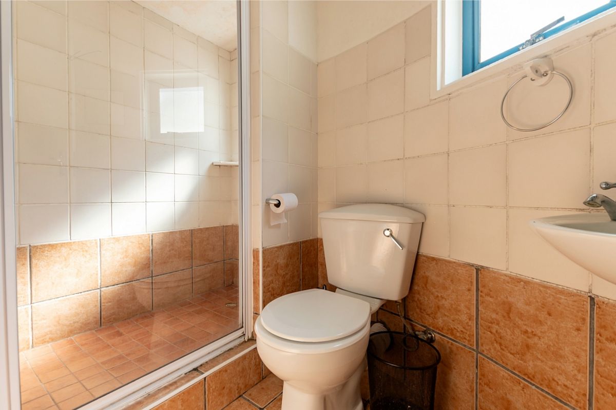 A compact bathroom featuring a shower enclosure, toilet, and wall-mounted basin with dated tiled finishes throughout.