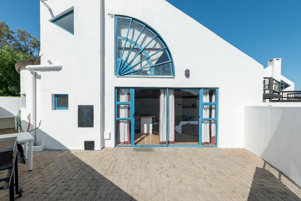 Rear exterior view of the property featuring a paved patio area, blue-framed sliding glass doors, and a distinctive fanlight window.