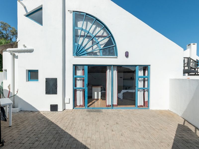 Rear exterior view of the property featuring a paved patio area, blue-framed sliding glass doors, and a distinctive fanlight window.