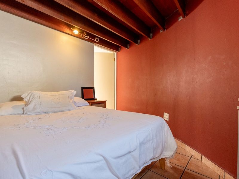 A bedroom featuring exposed timber ceiling beams, tiled flooring, and a distinct red accent wall.