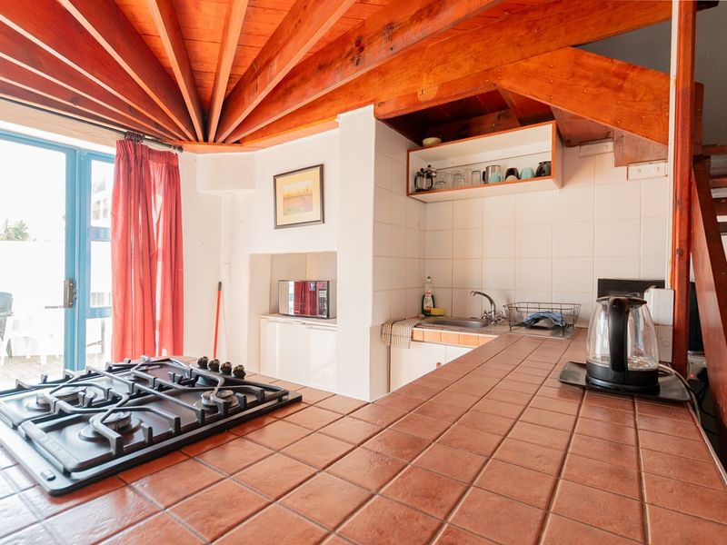 Compact kitchen featuring a tiled countertop, gas hob, stainless steel sink, and exposed timber ceiling beams with direct access to an outdoor patio area.