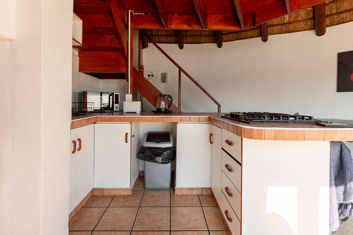 Compact kitchen featuring tiled countertops, built-in cabinetry, and a gas hob, situated beneath a wooden staircase with a traditional thatched ceiling.