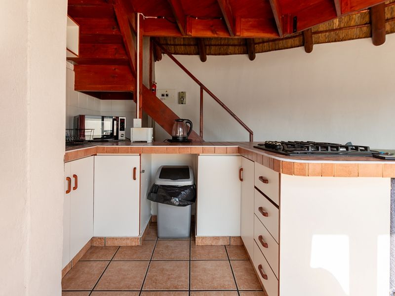 Compact kitchen featuring tiled countertops, built-in cabinetry, and a gas hob, situated beneath a wooden staircase with a traditional thatched ceiling.
