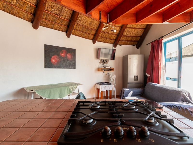 Open plan living area featuring a tiled kitchen island with a built-in gas hob, exposed timber rafters, and a traditional thatched ceiling.