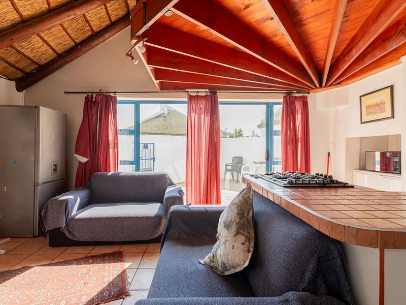 Open-plan living area featuring an exposed timber ceiling, tiled kitchen counter with integrated gas hob, and sliding doors leading to an outdoor patio.