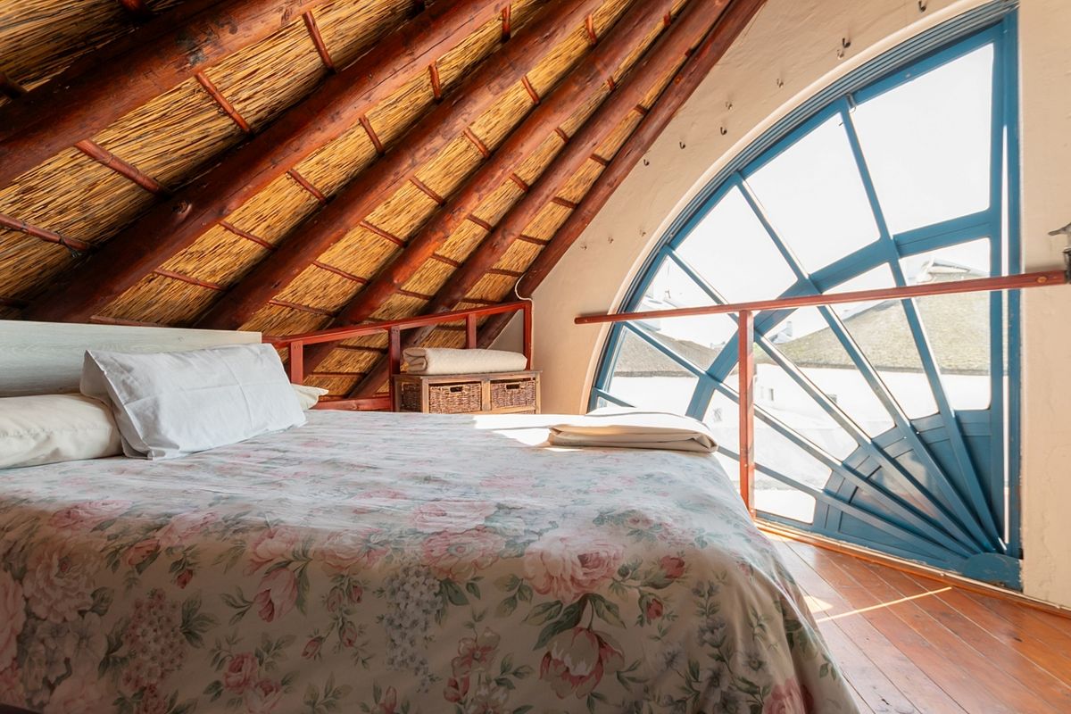 Unique loft-style bedroom featuring exposed timber rafters, a traditional thatched roof, and a large arched window providing ample natural light.