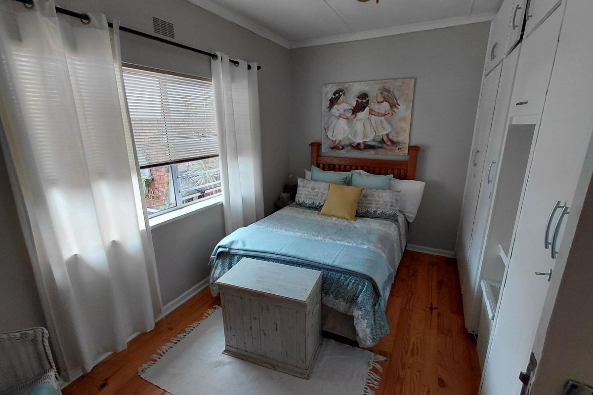 A cozy bedroom featuring polished timber flooring, built-in storage cupboards, and natural light through a window fitted with venetian blinds.