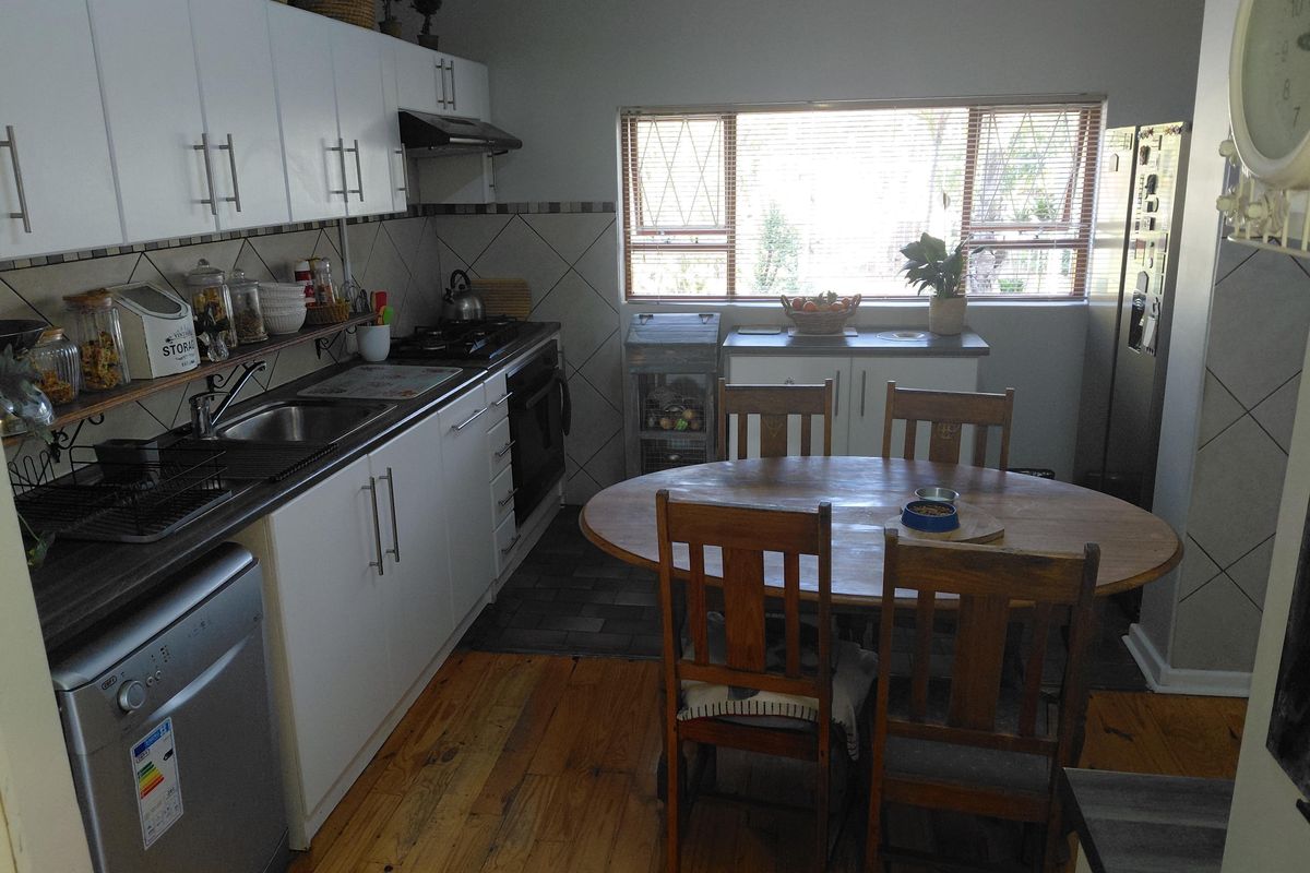 A functional kitchen featuring white cabinetry, dark laminate countertops, a gas hob, and timber flooring, with an integrated dining area.