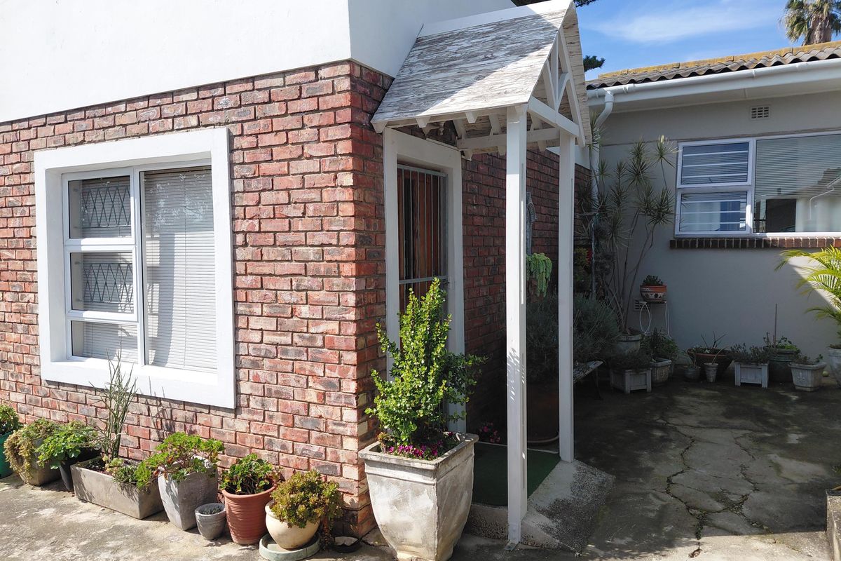 Rear exterior view of the property featuring a brick facade, a small covered entrance canopy, and concrete paved outdoor area.