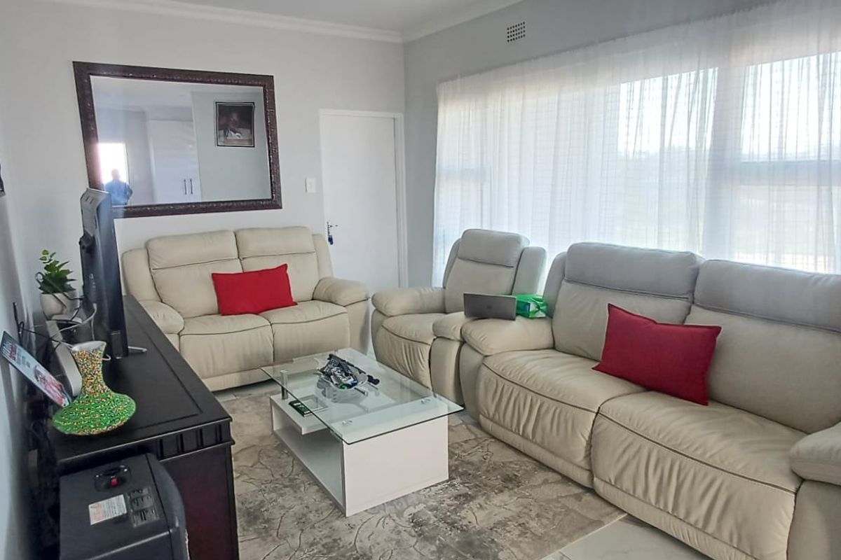 A comfortable living room featuring neutral walls, large windows with sheer curtains, and decorative cornice detailing.