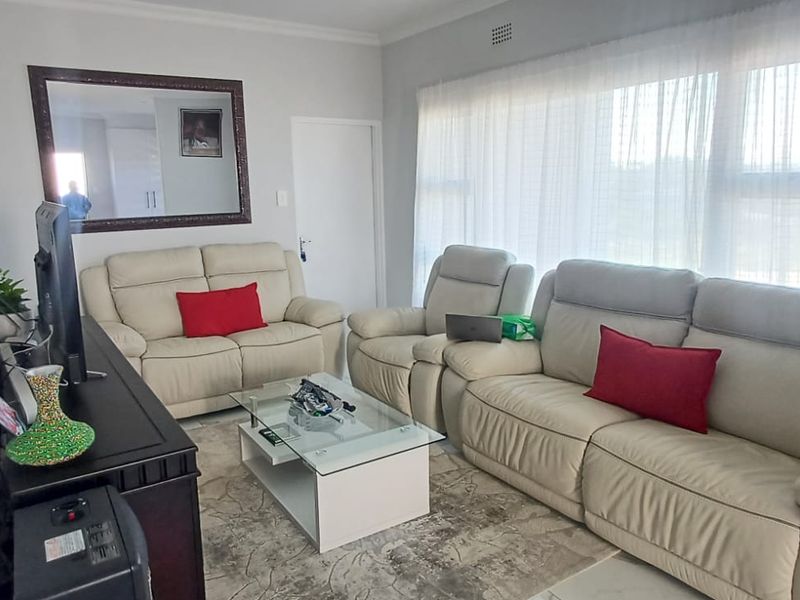 A comfortable living room featuring neutral walls, large windows with sheer curtains, and decorative cornice detailing.