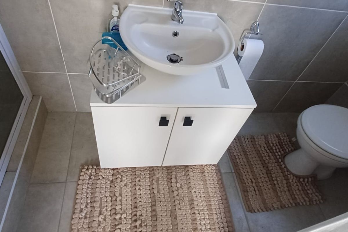 A clean and functional bathroom featuring a modern vanity cabinet with a ceramic basin, a toilet, and a glass-enclosed shower with neutral wall tiling.