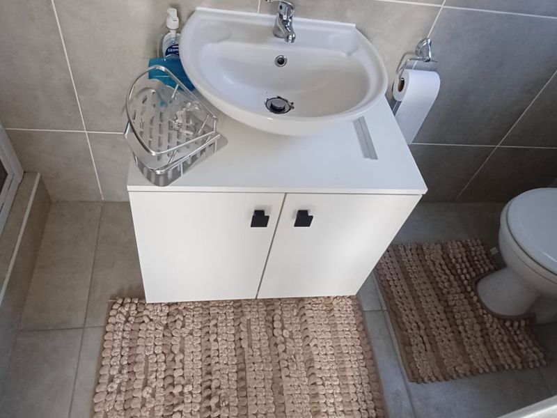 A clean and functional bathroom featuring a modern vanity cabinet with a ceramic basin, a toilet, and a glass-enclosed shower with neutral wall tiling.