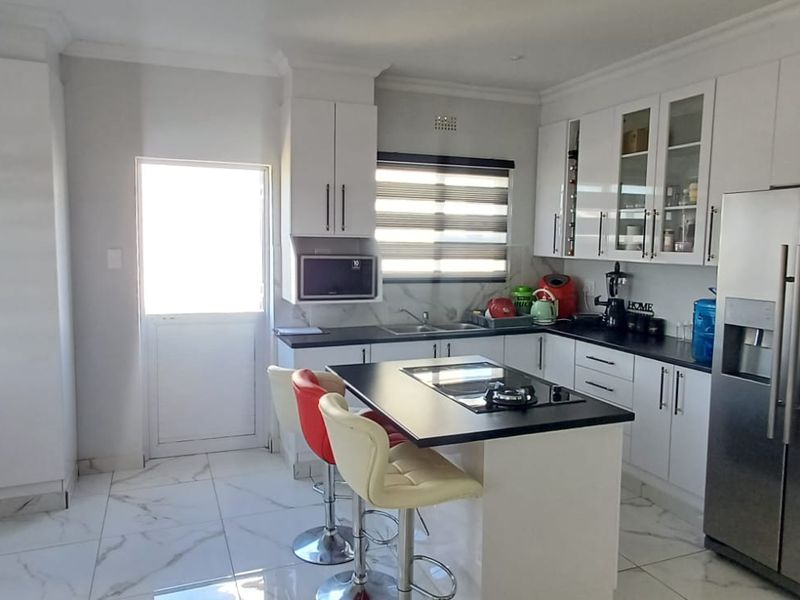 Modern kitchen featuring white cabinetry, a central island with a gas hob, marble-look tiled flooring, and ample storage space.