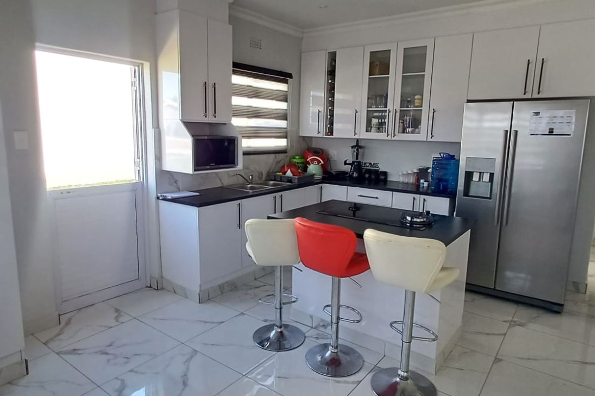 Modern kitchen featuring white cabinetry, dark stone countertops, a central island with a built-in hob, and polished marble-look floor tiles.
