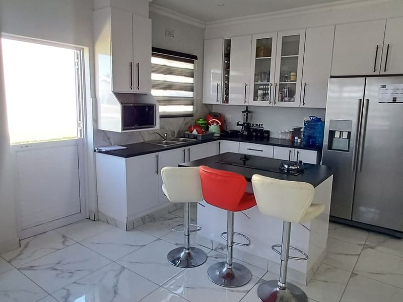 Modern kitchen featuring white cabinetry, dark stone countertops, a central island with a built-in hob, and polished marble-look floor tiles.