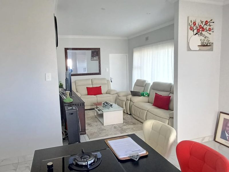 An open-plan living area featuring tiled flooring, recessed lighting, and a modern kitchen island with a built-in hob, seamlessly connecting to the lounge space.