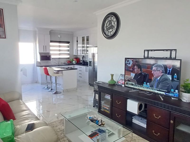 An open-plan living and kitchen area featuring modern cabinetry, a central kitchen island, and polished tiled flooring throughout the space.