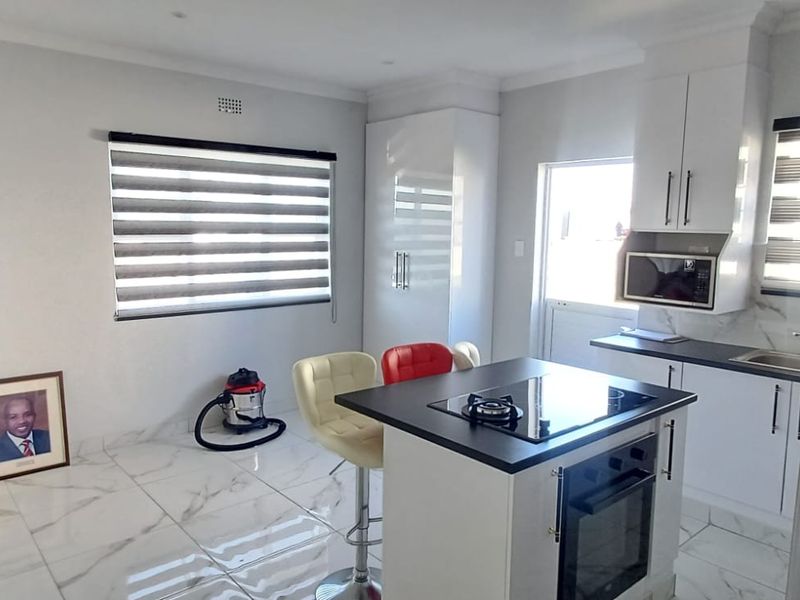Modern open-plan kitchen featuring a central island with a built-in oven and gas hob, complemented by sleek white cabinetry and marble-look floor tiles.
