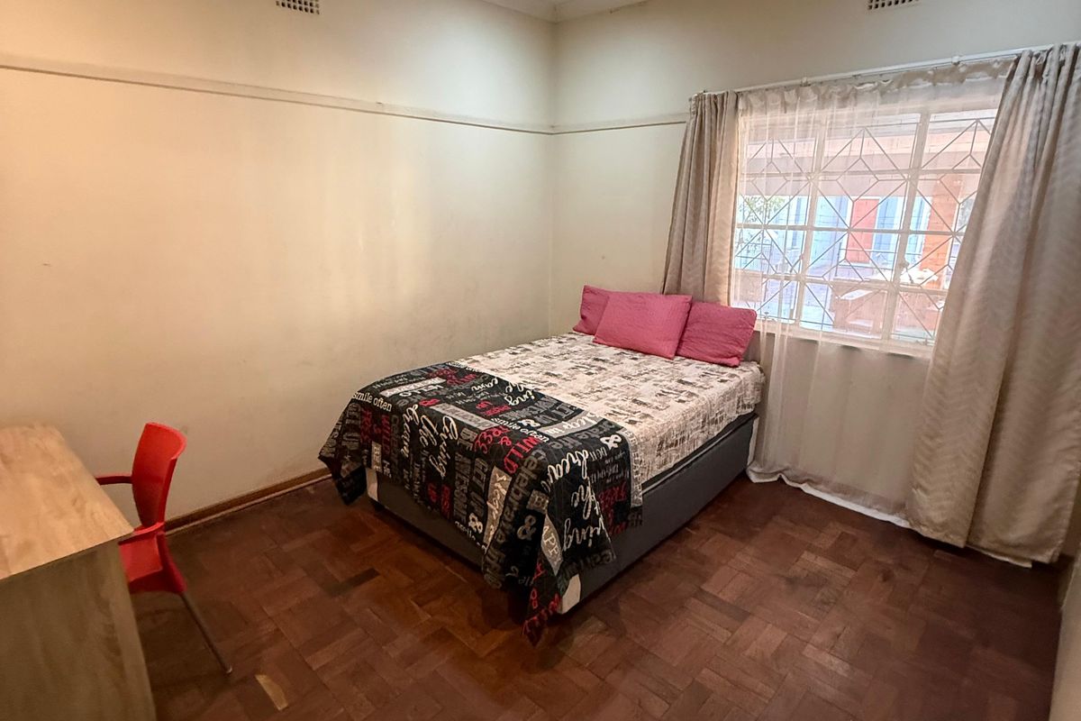 A bedroom featuring classic parquet flooring, picture rails, and security bars on the window, offering a functional space with potential for cosmetic updates.