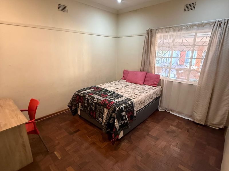 A bedroom featuring classic parquet flooring, picture rails, and security bars on the window, offering a functional space with potential for cosmetic updates.