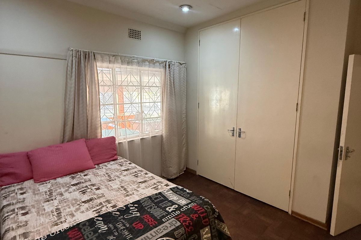 A bedroom featuring parquet flooring, built-in cupboards, and recessed downlights. The room includes security burglar bars on the window.