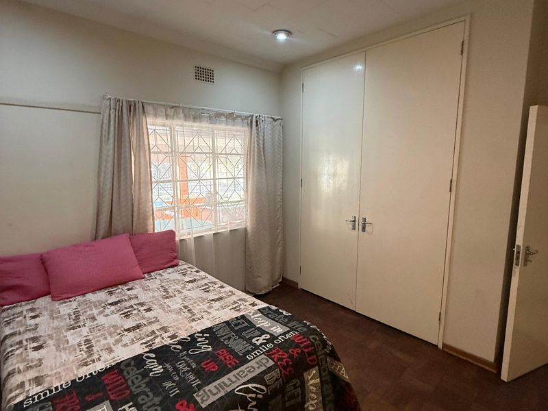A bedroom featuring parquet flooring, built-in cupboards, and recessed downlights. The room includes security burglar bars on the window.
