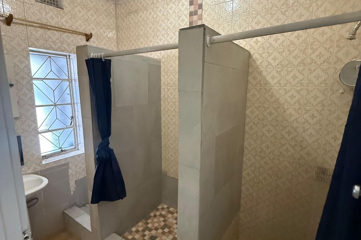 A functional bathroom featuring dual shower stalls with tiled finishes, a wall-mounted basin, and a window with security bars.