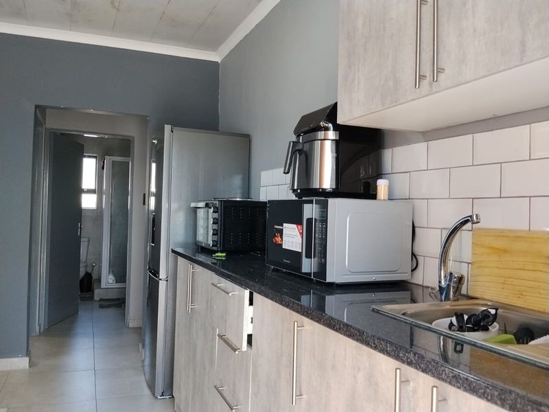 A functional kitchen featuring modern grey cabinetry, granite countertops, subway tile backsplash, and tiled flooring, with a view into the adjacent bathroom.