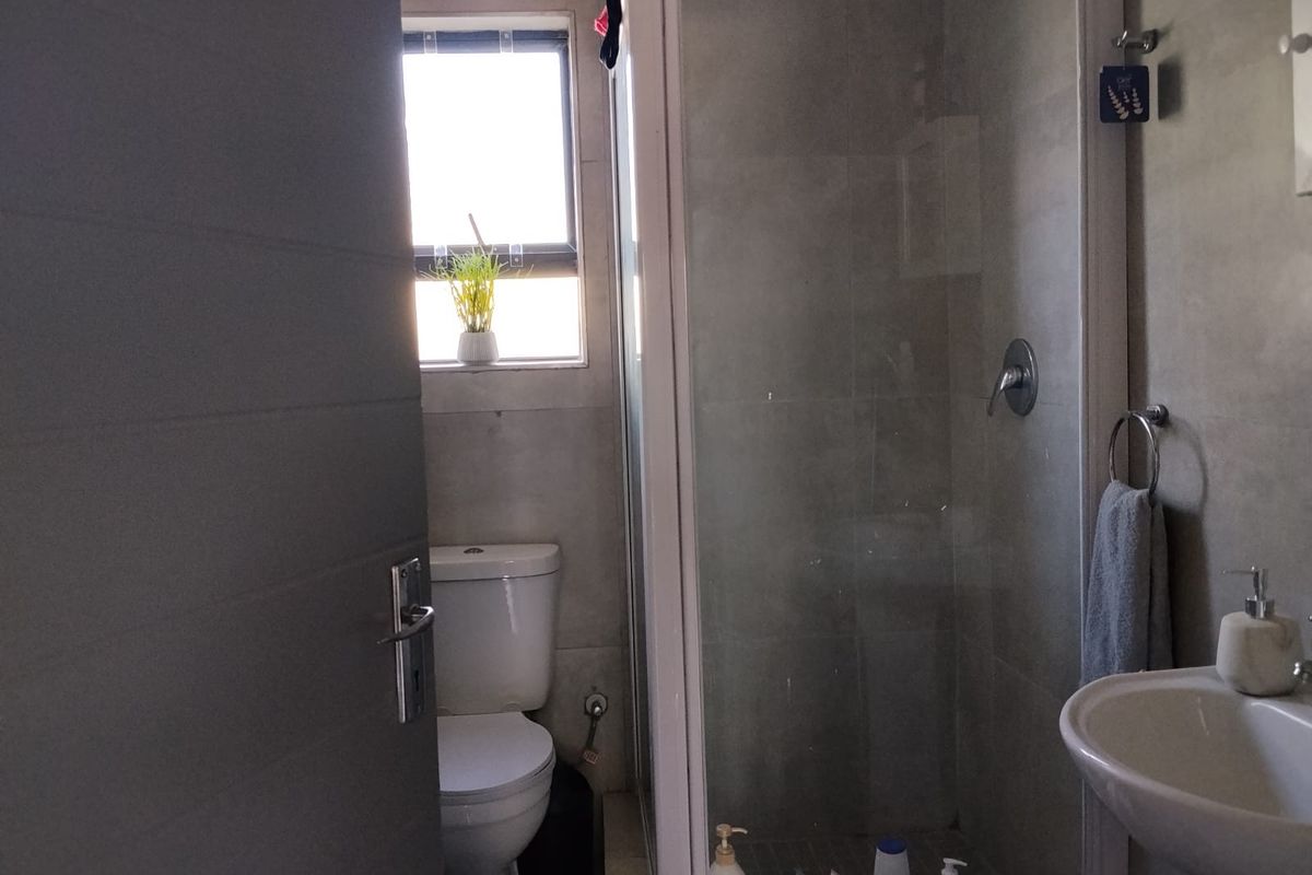 A functional bathroom featuring a glass-enclosed shower, pedestal basin, and toilet with neutral wall and floor tiling.