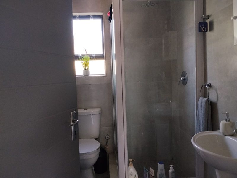A functional bathroom featuring a glass-enclosed shower, pedestal basin, and toilet with neutral wall and floor tiling.