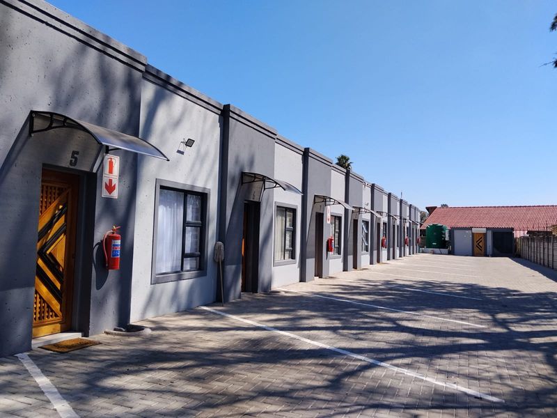 Exterior view of a row of modern flat units featuring paved parking, security doors, and individual entrance canopies.