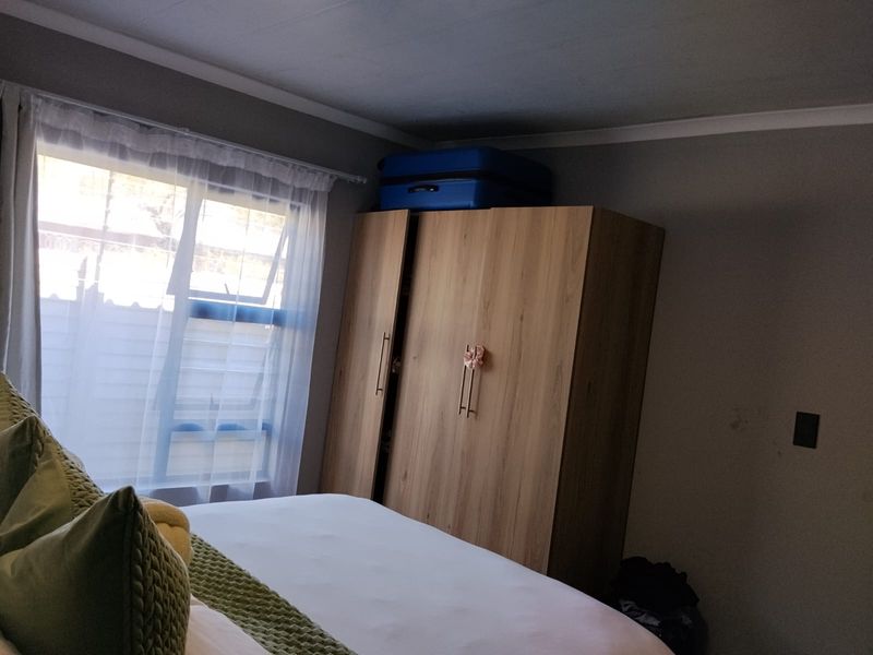 A bedroom featuring a built-in wooden wardrobe and a window with sheer curtains.