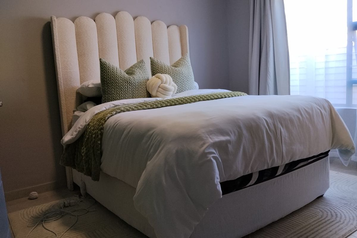 A well-maintained bedroom featuring neutral wall tones, laminate flooring, and natural light provided by a window with installed curtain tracks.