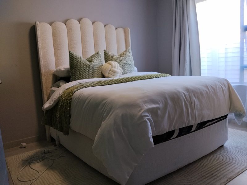 A well-maintained bedroom featuring neutral wall tones, laminate flooring, and natural light provided by a window with installed curtain tracks.