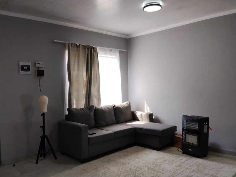 A living room featuring grey walls, a ceiling light fixture, and a window with curtain rod, providing a neutral base for interior design.