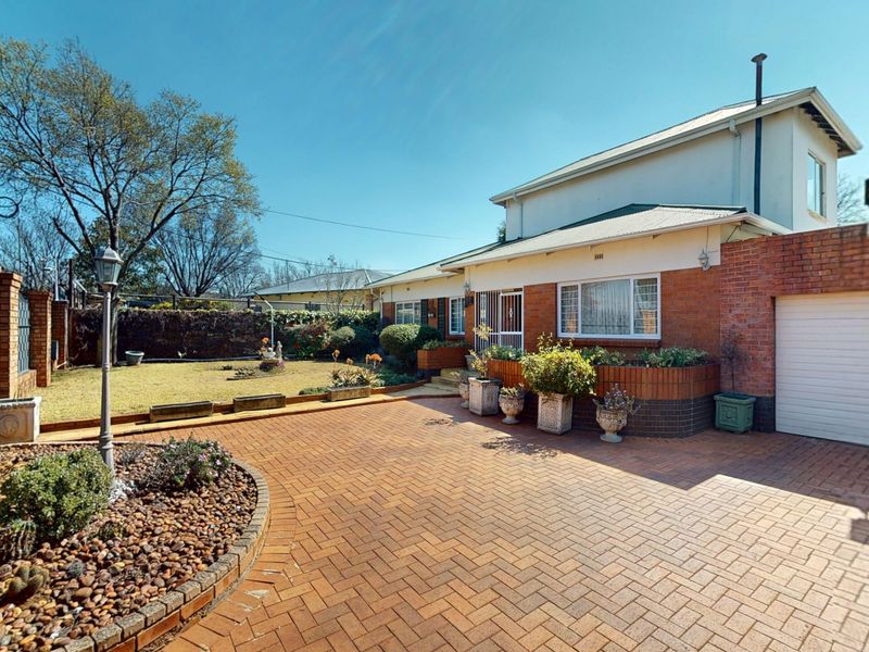 Front exterior view of the house featuring a paved brick driveway, attached garage, and landscaped garden area with brick boundary walls.