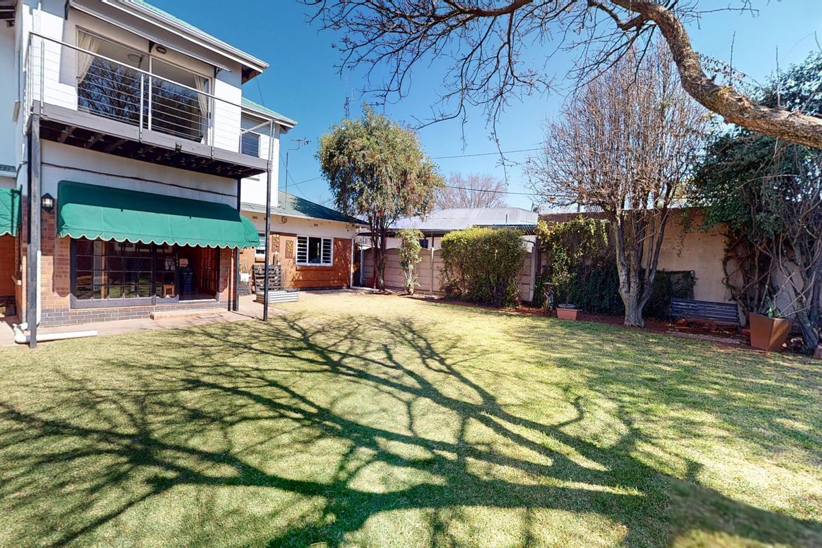 Rear view of the property featuring a spacious lawn, a ground-floor patio with a retractable awning, and an upper-level balcony.