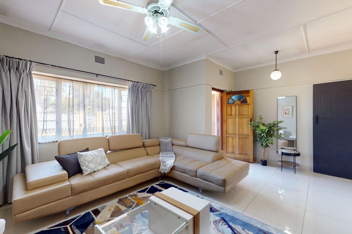 A bright and spacious living room featuring large windows, tiled flooring, and a ceiling fan, offering a comfortable and well-maintained living space.