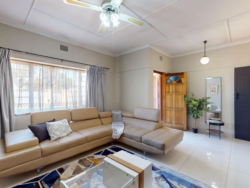 A bright and spacious living room featuring large windows, tiled flooring, and a ceiling fan, offering a comfortable and well-maintained living space.