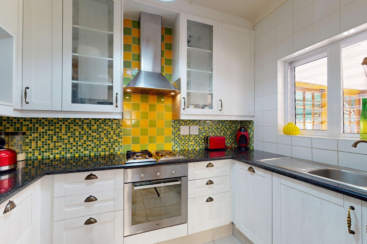 A functional kitchen featuring white cabinetry, granite countertops, a stainless steel oven, gas cooktop, and a vibrant mosaic tile backsplash.