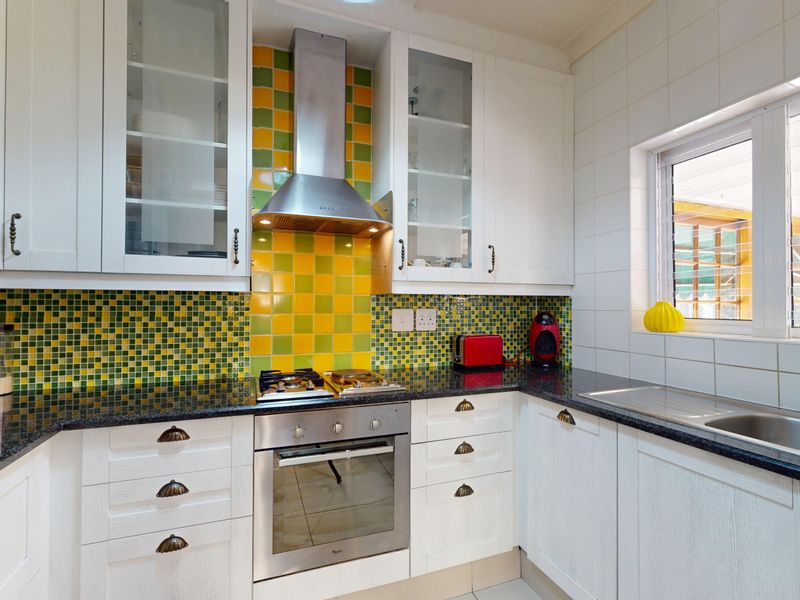 A functional kitchen featuring white cabinetry, granite countertops, a stainless steel oven, gas cooktop, and a vibrant mosaic tile backsplash.