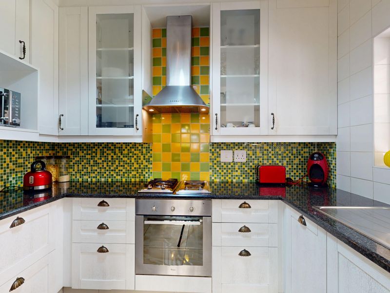 A functional kitchen featuring white cabinetry, granite countertops, and a vibrant mosaic tile backsplash with integrated stainless steel oven and hob.