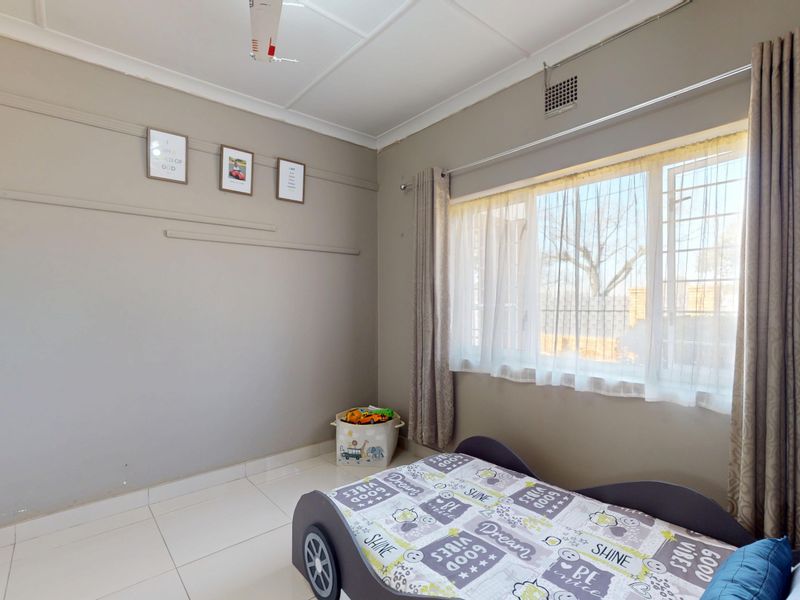 A bedroom featuring tiled flooring, a built-in wardrobe, and a window fitted with security bars, providing a functional and well-lit living space.