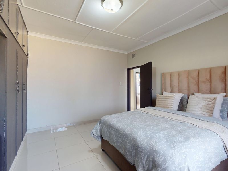 A well-lit bedroom featuring tiled flooring, built-in cupboards with mirrored accents, and classic ceiling detailing.